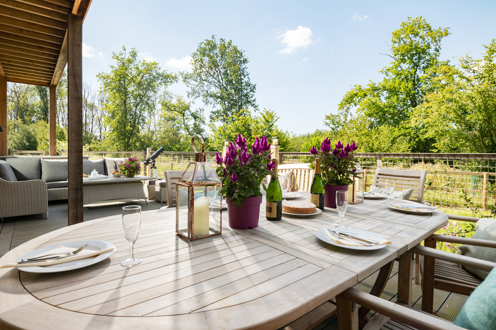 Deck area at Scots Pine holiday house in Hampshire, with teak dining table and chairs, and rattan furniture