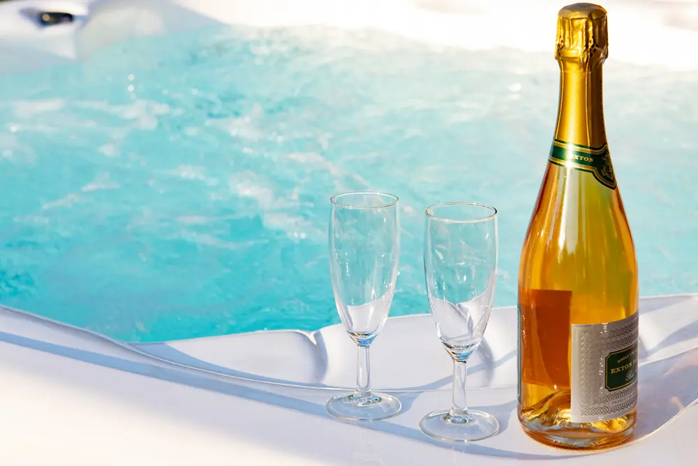 Hot tub in the garden with a bottle of pink bubbly and two champagne flutes on the side